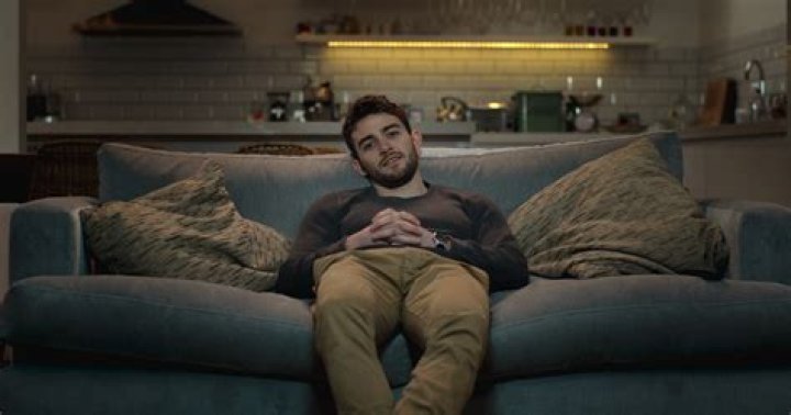 Connor sitting on a couch, arm on his knee in a scene from Succession.