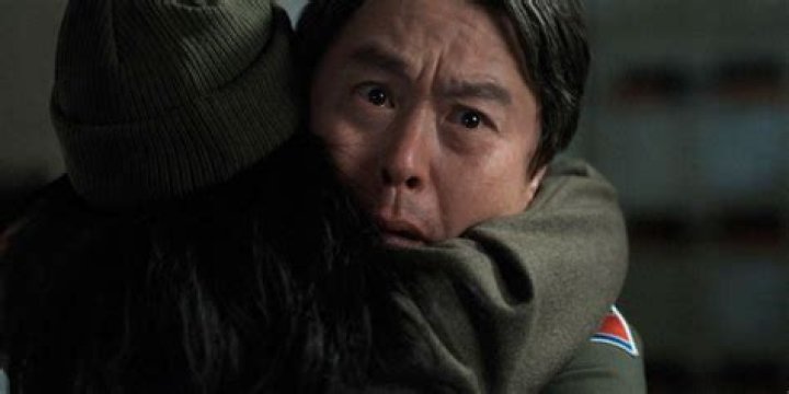 Lee hugs his wife and looks surprised by something off-camera