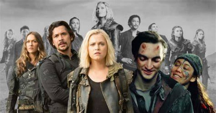 The 100 cast standing on dead grass wearing shades of grey and black for a season 5 promo shoot